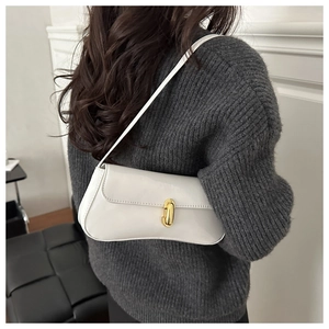 Modèle portant un sac baguette minimaliste en cuir verni crème sur un pull en maille