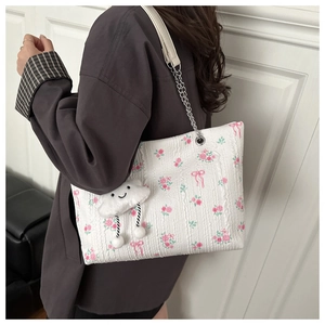 Detail of floral corduroy tote bag with bow prints and metal chain strap on model