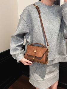 Sac à main en cuir marron mat avec boucle dorée porté à l'épaule par un mannequin