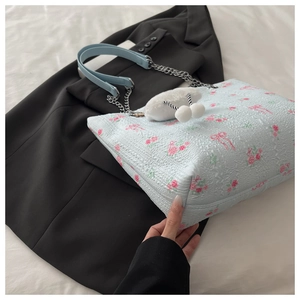 Detail of light blue floral tote bag with chain strap and white plush cherry charm