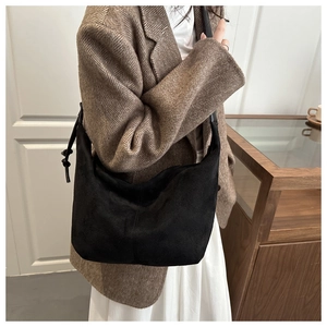 Detail of a black suede hobo bag with a decorative knotted shoulder strap on a model