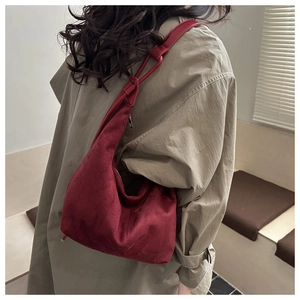Detail of burgundy suede crescent bag with adjustable strap worn over khaki coat