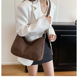 Close-up of a vintage brown matte suede shoulder bag worn with a white blazer