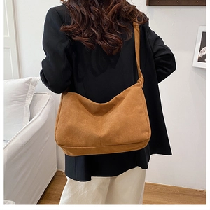 Brown suede-texture crescent crossbody bag shown on model in cozy home setting