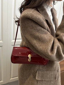 Sac baguette en cuir verni rouge foncé avec fermoir doré porté par un mannequin