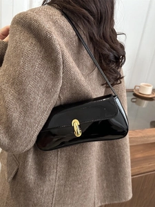 Sac sous l'aisselle noir brillant avec boucle dorée en U porté par un mannequin