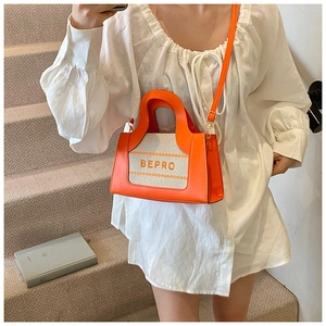 Detail of a mini orange and beige patchwork tote bag with embroidery on a white dress