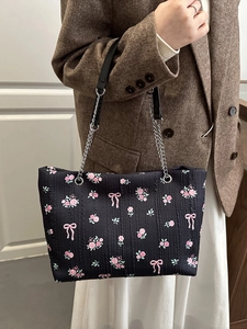 Fashionable black tote bag with rose patterns and bow details, shown on a model