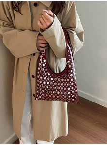 Detail view of burgundy crescent bag featuring silver rivets paired with a trench coat