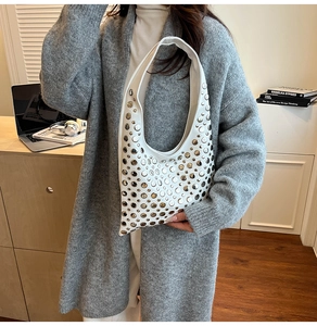 Close-up of a white leather hobo bag with silver rivets held by a model in a modern office