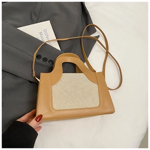 Detail view of stylish tan and cream crossbody bag on elegant fabric and blazer background