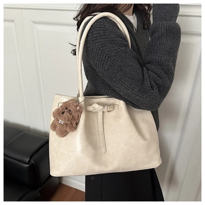 Detail of beige tote bag with matte faux leather texture and brown plush bear charm