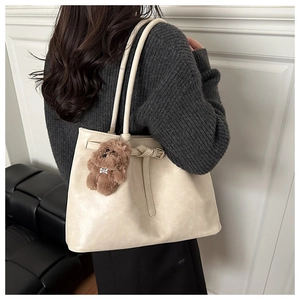 Detail of cream tote bag with pebble leather texture and plush dog charm on handle