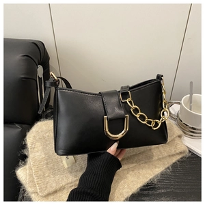 Détail du sac baguette en cuir noir avec grosse chaîne dorée et boucle métallique