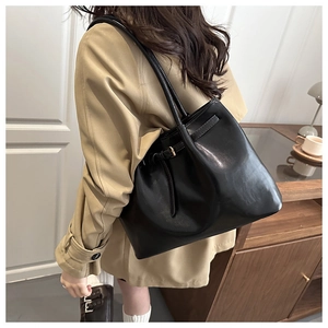 Detail of a large black vintage leather tote bag with decorative side buckle on a model