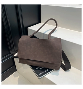 Deep brown matte suede messenger bag with round handle and wide fabric strap shown on a stand
