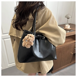 Detail of black faux leather tote bag with a brown plush teddy bear charm on shoulder strap