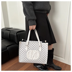 Close-up of white tote bag with gray M letter monogram print and oval logo detail