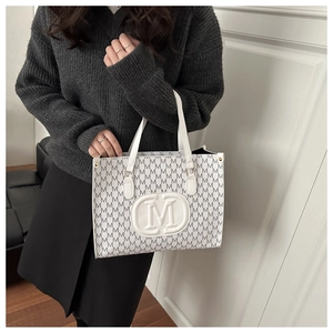 Close-up of white tote bag with all-over M-letter print and round embossed M logo