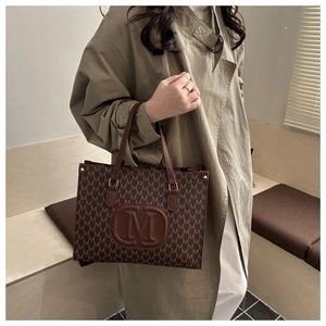 Detail view of brown tote bag with M-pattern print and embossed leather logo patch
