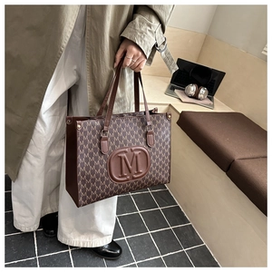Detail of a brown tote bag featuring all-over M-letter prints and embossed logo