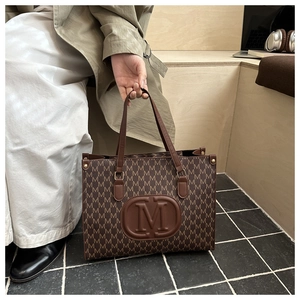 Detail view of large tote bag with M-letter prints and embossed emblem on the side
