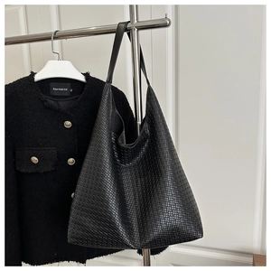 Gros plan du sac hobo en cuir tressé noir mat avec large bandoulière sur un cintre