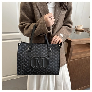 Close-up of black and grey patterned tote bag with M-logo leather patch and gold hardware