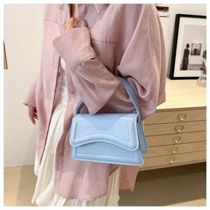 Close-up of light blue glossy handbag with wavy flap design on light pink shirt