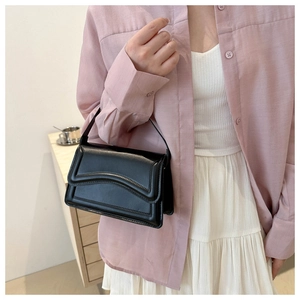 Close-up of a black minimalist shoulder bag with curved groove detail on a model