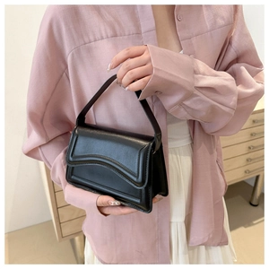 Detail of black underarm bag with wavy flap design held by a model in casual setting