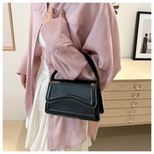 Detail of minimalist black shoulder bag with curved flap design and reinforced stitching