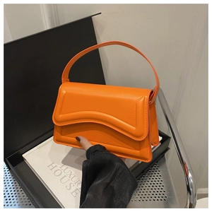 Detail of a bright orange structured handbag with a unique wavy edge flap and top handle