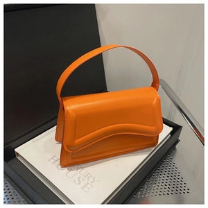 Detail of orange leather handbag with unique curved wavy flap design and wide handle