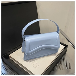 Detail view of a light blue faux leather handbag with curved flap on luxury book display