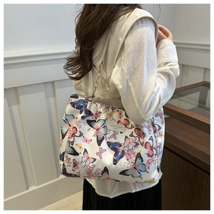 Detail of white tote bag with colorful butterfly prints and gold chain strap on shoulder