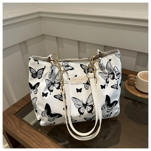 Detail of white tote bag featuring black butterfly patterns and gold chain link strap
