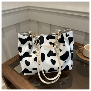 Close-up of cow print tote bag with gold chain details and faux leather handles