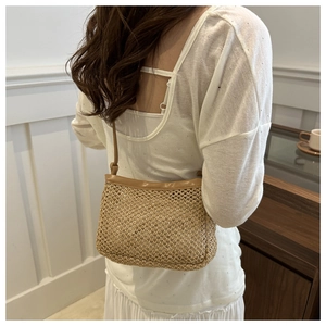 Brown woven straw crossbody bag with leather strap shown on a model's shoulder
