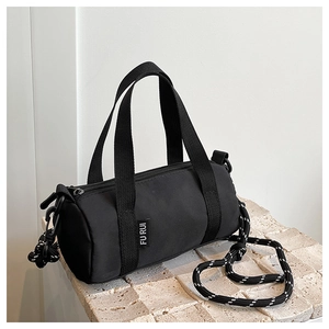 Détail du sac cylindrique noir minimaliste avec bandoulière tissée et étiquette en tissu
