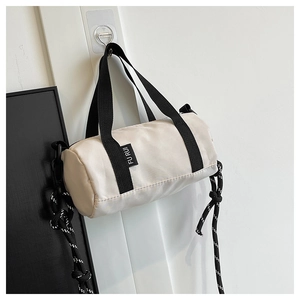 Détail du sac cylindrique en nylon blanc cassé avec sangles tissées et étiquette latérale