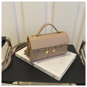 Detail of light brown rectangular handbag with golden zippers and decorative lock on a book