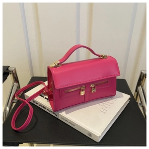 Detail of rose red crossbody bag with decorative zippers and golden padlock on a white book