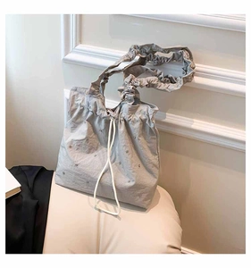 Detail of grey drawstring tote bag featuring silver studs and ruffled cloud handle straps