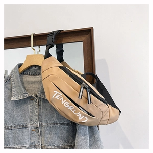 Detail of khaki nylon belt bag with white lettering and dual zippers against a denim jacket