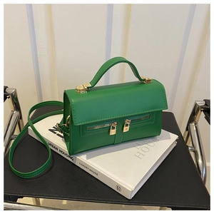 Detail of green minimalist handbag with gold metal lock and zipper on a luxury book