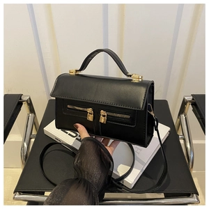 Detail view of the black leather handbag featuring dual gold zippers and lock accents