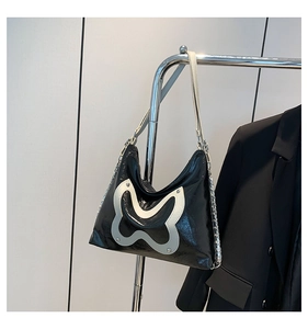 Detail of glossy black faux leather shoulder bag with white patchwork and silver chain