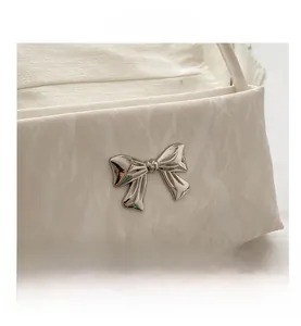 Close-up of creamy textured handbag featuring a delicate silver metal bow buckle detail
