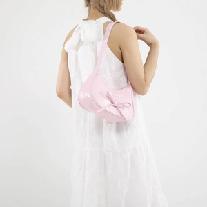 Pink crescent hobo bag with bow decoration shown on shoulder with white lace dress